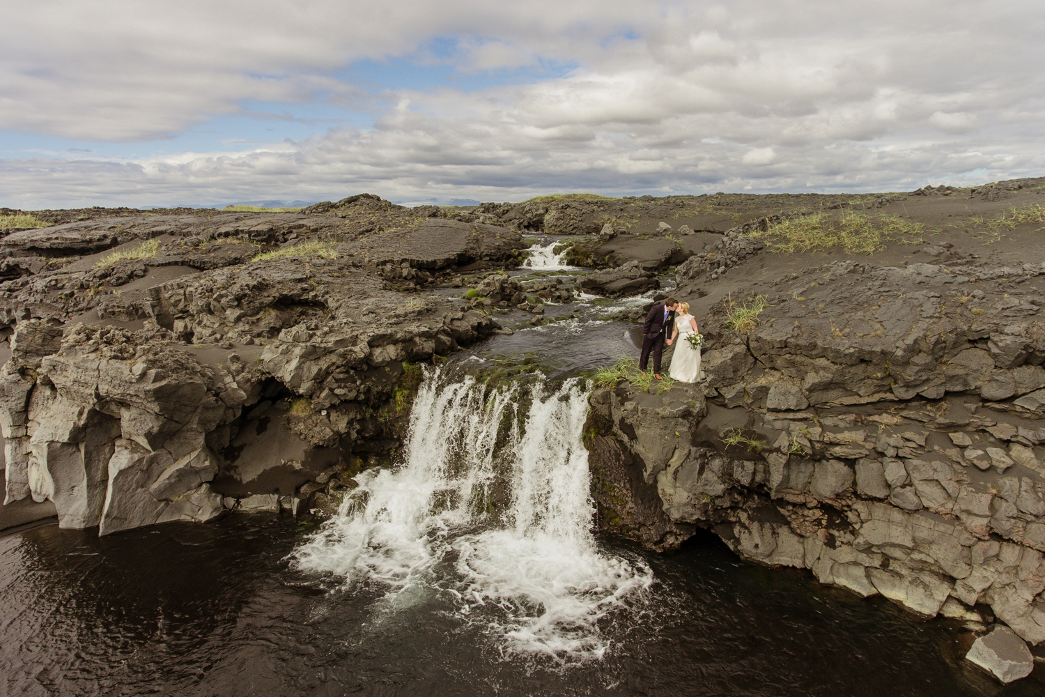 Rachel and John standing on top of a lava rock waterfall kissing in Iceland