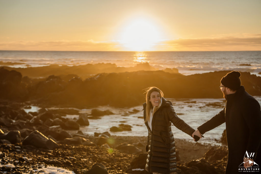 Iceland Engagement Couple walking on lava rock beach at sunset