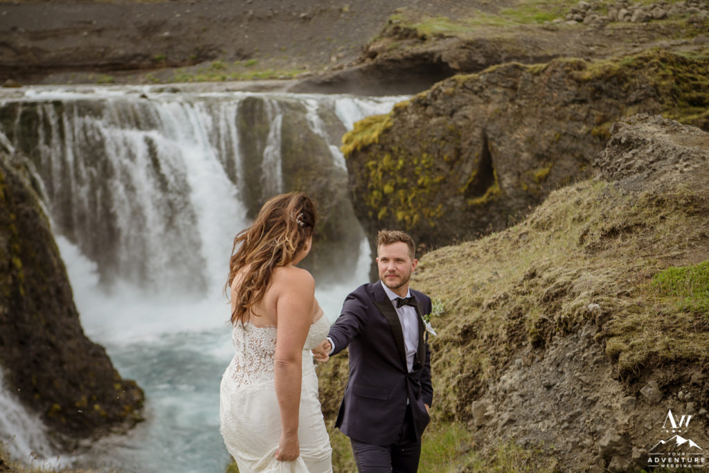 Groom leading his bride down to hidden waterfall